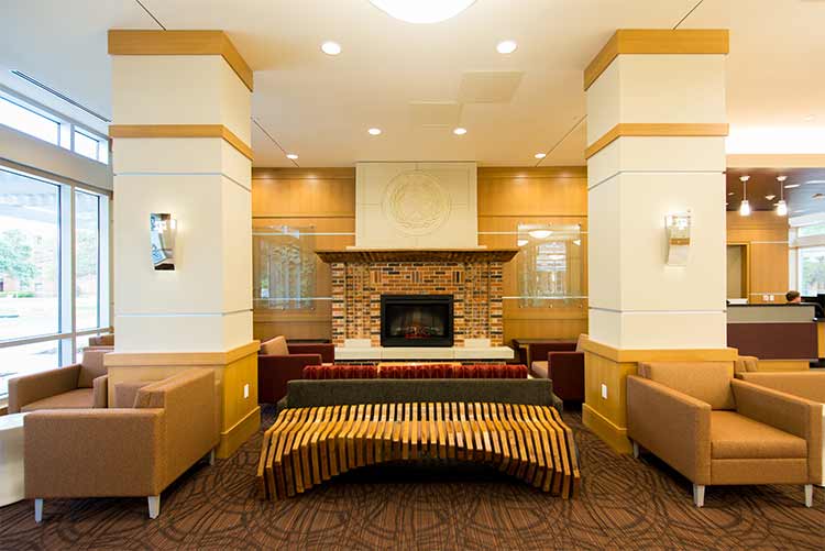 Hullabaloo Hall common area. One fireplace, six lounge chairs, one artistic, slotted coffee table, and North Area Office desk. 