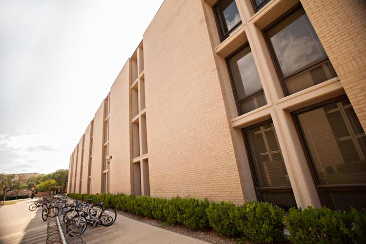 Exterior view of the side of Neeley Hall. Shows dorm room exterior windows and two bike racks. 