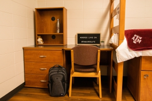 Commons hall dorm desk and chair,  alongside a dresser and book case. A book bag sites infant of the dresser.