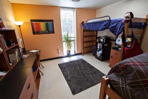 Interior of a decorated Aston Dorm Room. Two lofted beds are shown. Underneath on e of th lofted beds is a fridge and a TV.