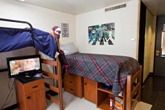 Interior of a decorated Aston dorm room. Two lofted twin beds are shown. Underneath one is a TV, the other has storage drawers underneath. An Texas A&M and a Beatles poster hang on the walls.