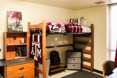 Interior of a decorated Dunn dorm. A lofted bed with A&M bedding is shown, with a shoe rack, laundry basket, and storage drawers underneath.  Next to the lofted bed is a desk, with a bookshelf on top.