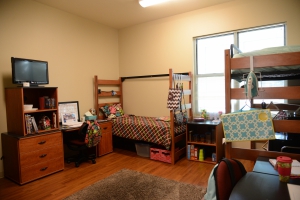 The interior of a Hullabaloo dorm. Three twin sized beds are shown, along with a desk, a TV, and other dorm furniture.