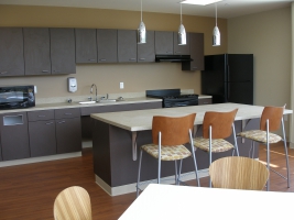 The interior of Hullabaloo kitchenette. Three chairs at the island, a microwave, and cabinets are shown.