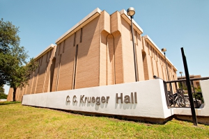 Exterior view of Kruger Hall with some trees, and the "CC Krueger Hall" sign in front of the building exterior.