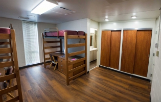 Empty Krueger dorm with two lofted twin sized beds, with desks and chairs underneath. A view of the closets and the bathroom are shown as well.