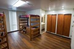 Empty Krueger dorm with two lofted twin sized beds, with desks and chairs underneath. A view of the closets and the bathroom are shown as well.