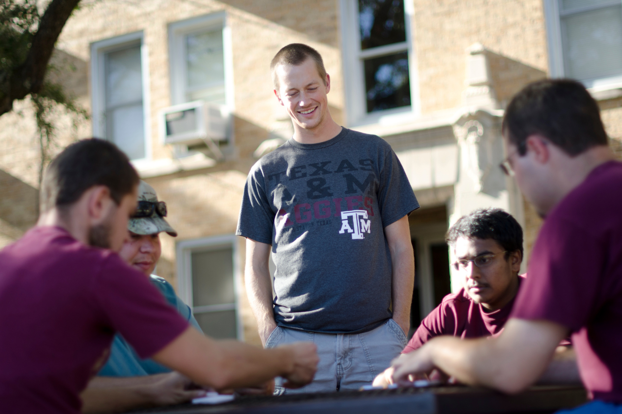 Four students sit a table, while a staff member stands over them and smiles.