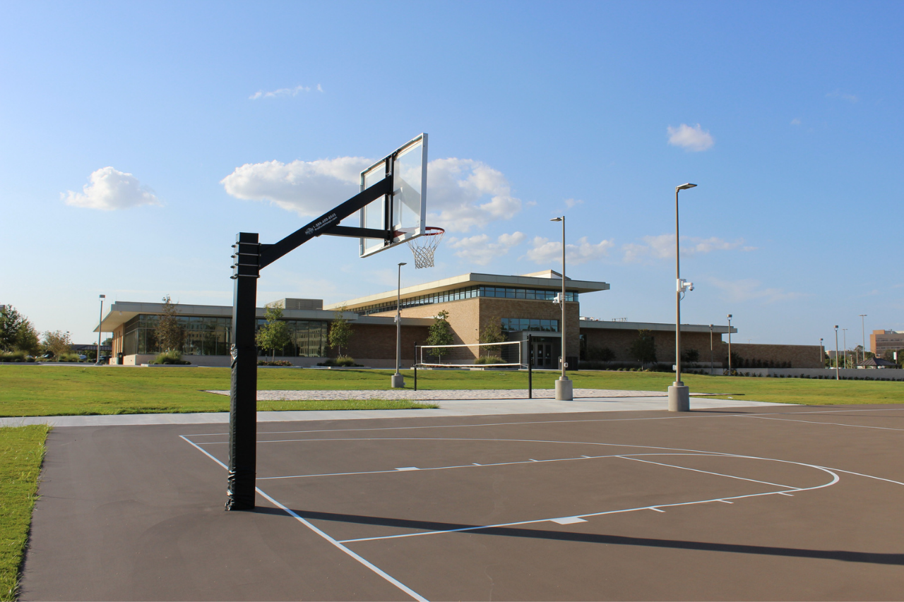 Empty basketball court outside. There is an empty sand volleyball court in the background.