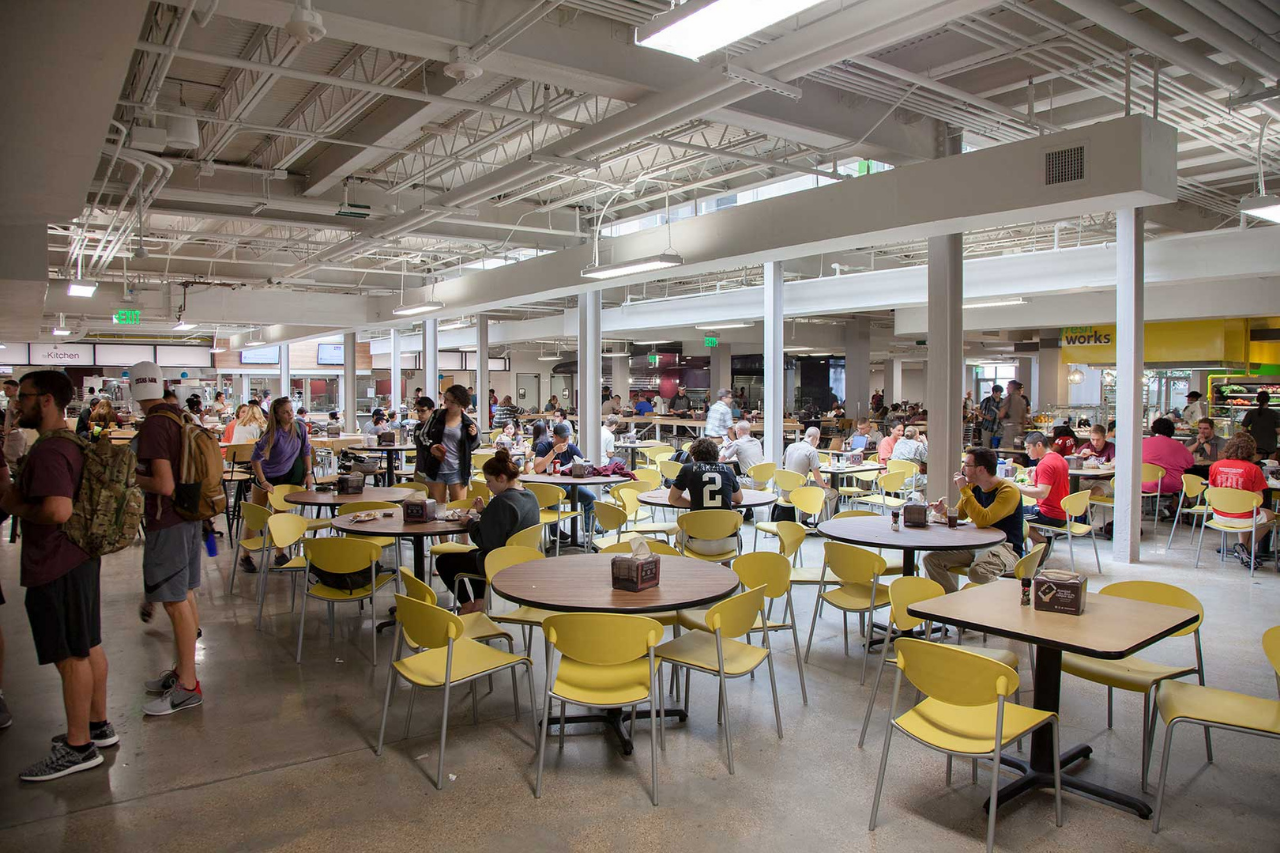 The Interior of a busy dining hall with students sitting and eating their meals, while other students wait in line at the various dining hall stations.