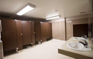 View of Community Bathroom. Four bathroom stalls are seen with two sinks.