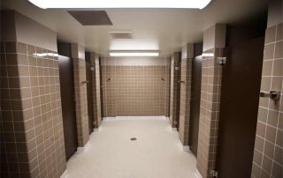 View of Community Bathroom. Multiple shower stalls are seen lined up in the bathroom.