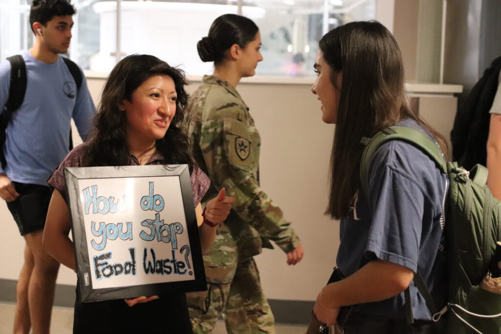 Two people talking, one is holding a sign that says "how do you stop food waste?"