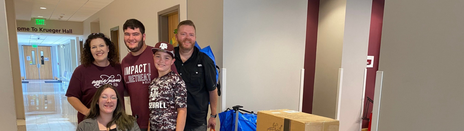 Family posing with a resident inside Krueger Residence Hall next to move in boxes