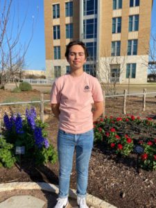 male student wearing pink shirt stands outside