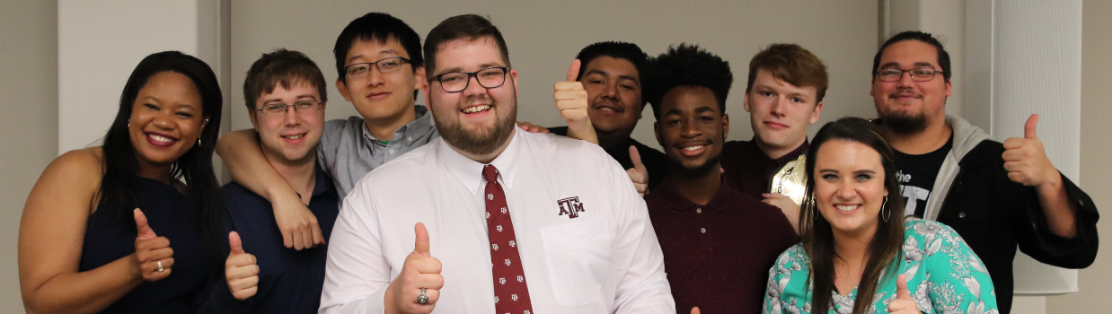 Students with a staff member in the front. They all throw up the gigem sign.