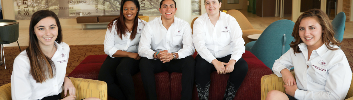 Five members of the Residential Housing Associations are seated and smiling at the camera, wearing white polos with the Residential Housing Association logo on it