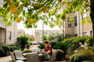 student sitting in gardens apartment outside